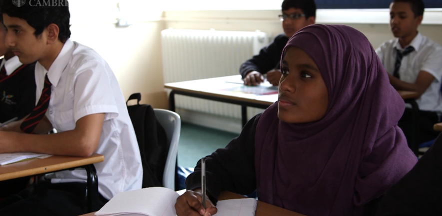 School girl wearing headscarf sitting at her desk in class