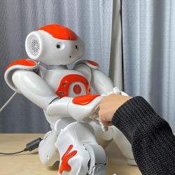 Photo of a researcher bumping fists with Nao, the robot helping assess mental wellbeing in children