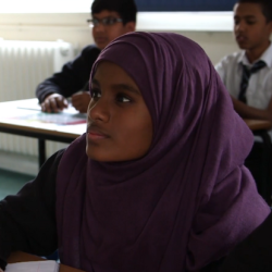 School girl wearing headscarf sitting at her desk in class